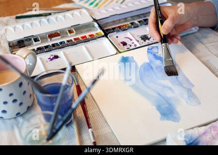 Mit Aquarellfarben malen - - Frau malt mit Aquarellpinsel einen blauen Hintergrund - Jena Atelier Deutschland *** Malerei mit Aquarellfarben Frau malt einen blauen Hintergrund mit einem Aquarellpinsel Jena Atelier Deutschland Stockfoto
