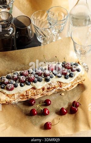 Blick von oben auf den Meringue-Rollkuchen mit Beeren auf Pergamentpapier. Rustikale, hausgemachte Dessert flach gelegt. Stockfoto