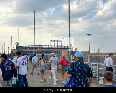 Queens, New Yoek, USA - 21. August 2025: Gruppen von Menschen gehen tagsüber auf einem Pfad zu einem Stadion. Stockfoto