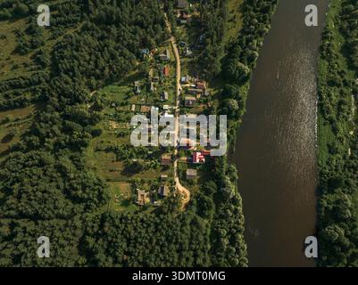Aus der Vogelperspektive eines kleinen Dorfes in der Nähe von Bereziwka oder Minsk, Weißrussland, mit bunten Häusern, Gärten, unbefestigten Straßen, ein dichter Wald und ein sich windender Fluss. Stockfoto