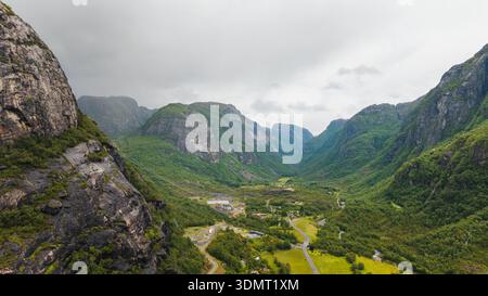 Aus der Vogelperspektive von Lysebotn, Norwegen, mit hohen Klippen, üppigen grünen Tälern, einer gewundenen Straße, verstreute Gebäude und ein bedeckter Himmel. Stockfoto