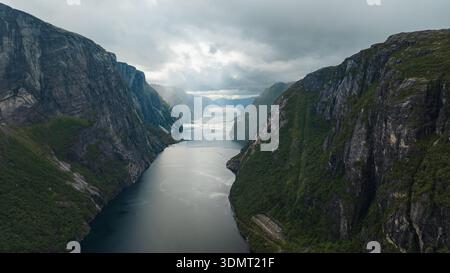 Dramatischer Blick auf den Lysefjord in Norwegen, mit steilen Klippen, ruhigem Wasser, grünen Flecken und einem kleinen Pfad entlang des Fjordes. Stockfoto