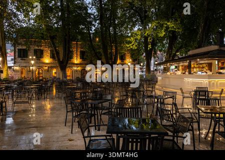 Trebinje, Bosnien und Herzegowina - 20. August 2022: Außenbereich eines leeren Cafés mit Tischen und Stühlen an einem regnerischen Abend. Stockfoto