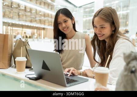 Junge asiatische Freundinnen, die Online-Shopping auf Laptop genießen Stockfoto
