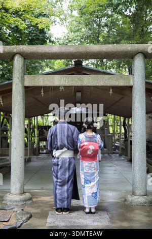 Ein Paar in Yukata steht vor einem Torii-Tor im Yasaka-Schrein. Kyoto, Japan. Stockfoto