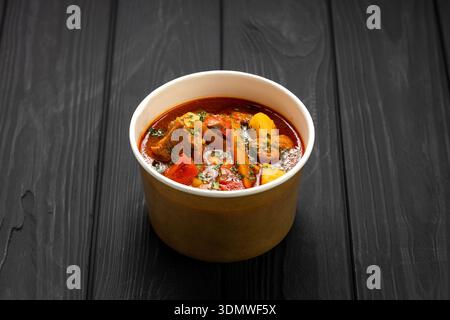 Ungarische Bohr-Gulasch-Suppe mit Rindfleisch und Gemüse in Kraftschale auf dunklem Holztisch Stockfoto