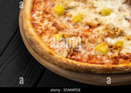 Hähnchenanaspizza mit geschmolzenem Mozzarella auf Holzbrett, dunkler Hintergrund Stockfoto