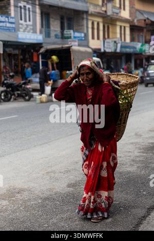 Kathmandu, Nepal – 15. März 2015: Ältere nepalesische Frau mit einem traditionellen Webkorb spaziert durch eine geschäftige Stadtstraße im städtischen Alltag. Stockfoto