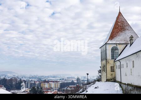 Eine ruhige Winterszene mit einem schneebedeckten Kirchturm auf einem Hügel mit Blick auf ein ruhiges Dorf. Bewölkter Himmel, ferne Häuser, und friedlich, se Stockfoto