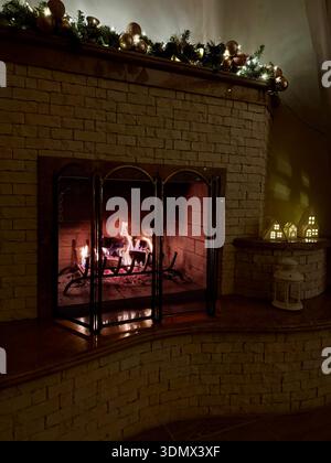 Warme Szene eines Kaminmantels mit Girlande, Lichtern und gemütlichem Kamin. Stockfoto