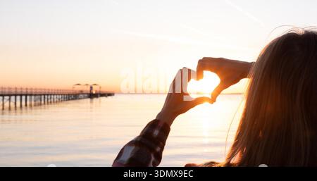 Hände bilden eine Herzform mit einer Silhouette bei Sonnenuntergang am Strand || Model veröffentlicht Stockfoto