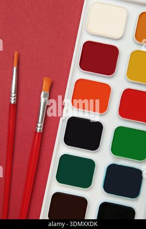 Aquarellfarben malen auf rotem Hintergrund. Zubehör für Zeichnen und Kreativität. Leerzeichen für Text Stockfoto