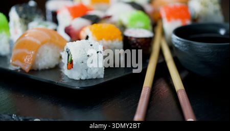 Sushi-Brötchen werden auf einem schwarzen Teller mit Essstäbchen an einem Esstisch angeordnet Stockfoto