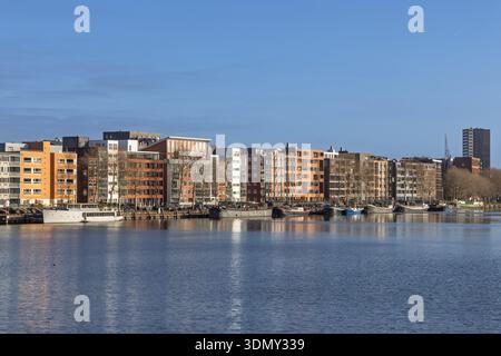Farbenfrohe moderne Wohnhäuser und Hausboote in Java-eiland in Amsterdam mit architektonischen Reflexen auf dem ruhigen Wasser des IJ-Flusses. Stockfoto