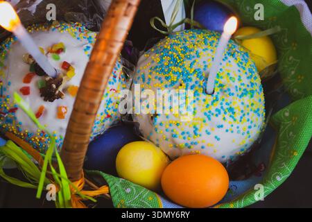 Osterkuchen mit bemalten Eiern und Kerzen in einem Korb. Osterstillleben. Orthodoxe Eater-Feier. Bunte Ostereier mit süßem Kuchen im Korb Stockfoto