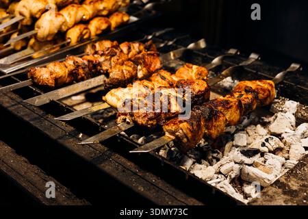 Saftige, gewürzte Fleischspieße grillen über heißen Kohlen an einem Street Food Stand. Das appetitliche Aroma von gebratenem Huhn und Rindfleisch erfüllt die Luft und lädt zu Fo ein Stockfoto