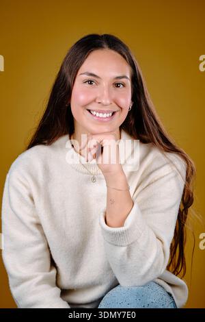 Lächelnde junge Frau posiert mit dem Kinn auf der Hand in einem Studio-Porträt Stockfoto