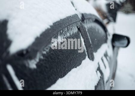 Ein Auto ist stark mit Schnee und Eis bedeckt, gefroren in einer Winterlandschaft. Das Fahrzeug steht im Freien und wird durch Frostschichten blockiert, die das h reflektieren Stockfoto