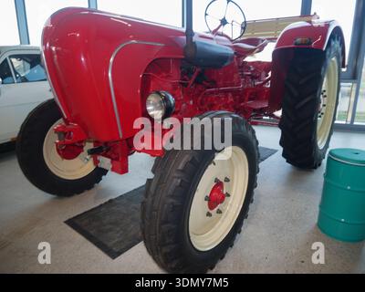 Der rote Vintage-Traktor mit markanten Reifen wird in Innenräumen ausgestellt und hebt das klassische Design und die mechanischen Merkmale in einer geräumigen Umgebung hervor Stockfoto