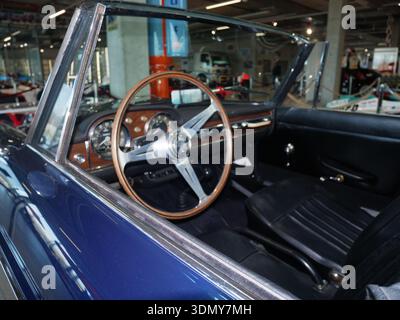 Innenansicht eines klassischen Cabriolets mit Holzlenkrad, schwarzen Ledersitzen und Armaturenbrettanzeigen in einer Garage Stockfoto