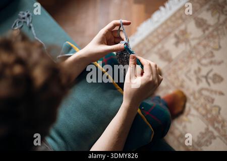 Nahaufnahme einer Person, die in gemütlicher Umgebung mit grauem Garn häkelt. Die Hände arbeiten geschickt mit einer Häkelnadel und zeigen Konzentration und Konzentration Stockfoto
