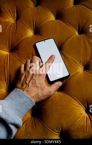 Eine Hand interagiert mit einem Smartphone, dessen Bildschirm beleuchtet wird, während sie auf einer luxuriös strukturierten Samtoberfläche aufliegt und eine Mischung aus Technologie hervorhebt Stockfoto