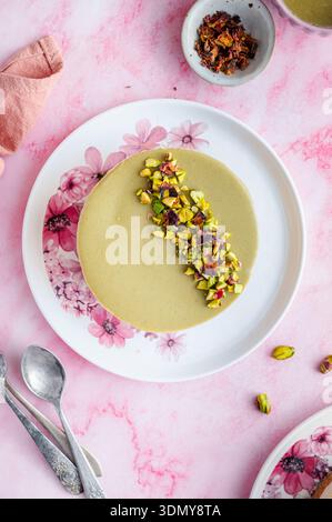 Ein köstlicher Käsekuchen mit Pistazien und weißer Schokolade, elegant präsentiert auf einem Blumenteller. Garniert mit zerstoßenen Pistazien, bietet er eine perfekte Mischung Stockfoto