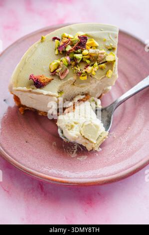 Eine köstliche Scheibe Pistazien und Käsekuchen aus weißer Schokolade, garniert mit zerstoßenen Pistazien. Perfekt cremig und verwöhnend, elegant präsentiert Stockfoto