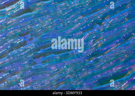 Eine faszinierende holographische Glasoberfläche mit geprägtem Muster, die einen gewebten Effekt mit einem lebendigen Spektrum von Blau, Violett und Schimmelfarben erzeugt Stockfoto