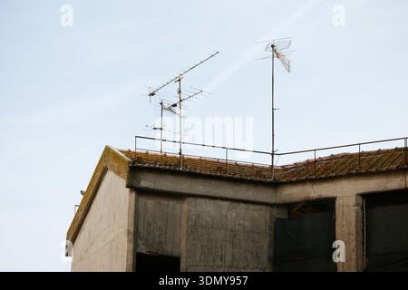 Bild von Dachantennen, die hoch vor einem klaren blauen Himmel stehen. Diese Antennen befinden sich auf einem Betondach, was auf traditionelle Rundfunkanlagen hinweist Stockfoto