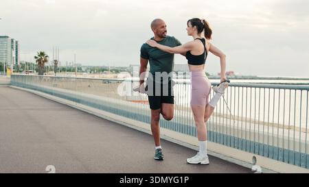 Ein multiethnisches Paar junger Menschen, die im Sommer gemeinsam trainieren, männliche und weibliche Athleten, die Muskeln dehnen, Übungen am Meer, sportliche Pässe machen Stockfoto