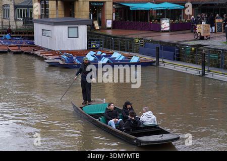 Punter steuert einen traditionellen Punt mit Passagieren auf dem schlammigen Fluss Cam in Cambridge an einem Wintertag. Cambridge, England Stockfoto