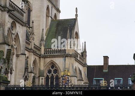 Gotische Kapelle außerhalb des St John's College Cambridge mit verzierten goldenen Wappen und spitzen Bögen unter bedecktem Himmel. Cambridge, England Stockfoto