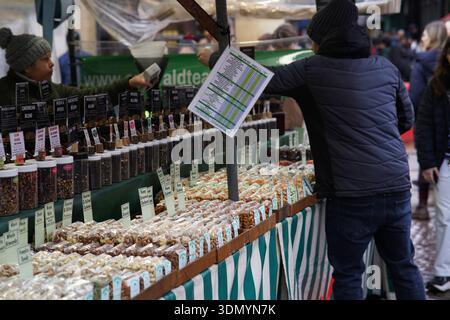 Anbieter zeigt Gewürztabelle an einem Marktstand mit Gläsern mit losen Gewürzen, Kräutern und Nüssen in Cambridge. Cambridge, England Stockfoto