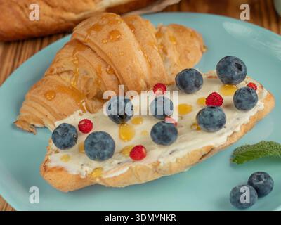 Frisches Croissant mit Cream Cheese, Heidelbeeren und Honig. Croissant-Füllungsidee Stockfoto