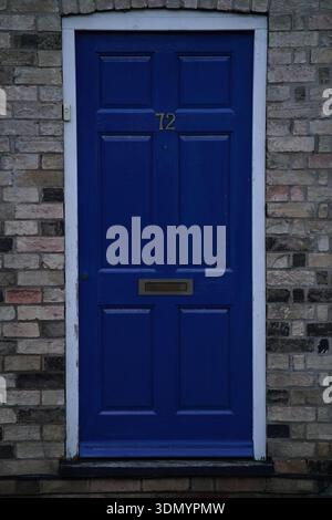 Leuchtend blaue Haustür Nummer 72 an der historischen Backsteinfassade in Cambridge. Cambridge, England Stockfoto