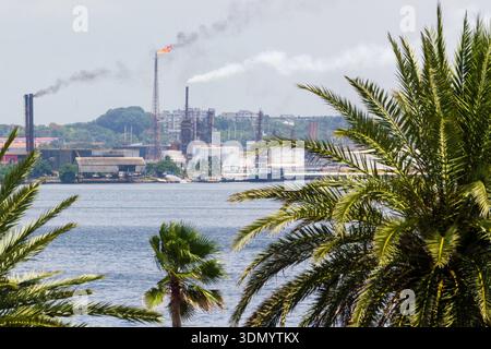 Ein malerischer Blick auf ein Industriegebiet auf der anderen Seite des Wassers, umgeben von tropischen Palmen. Stockfoto