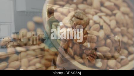Eine kleine Tasse schlürft, eine ältere Frau in einem leichten Pullover, die ihr Telefon in der Küche mit Kaffeebohnen-Overlay hält Stockfoto