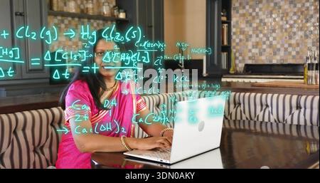 Eine reife indische Frau in rosa Sari mit Armreifen im Küchenkaffee, die Laptopgleichungen zeigt Stockfoto