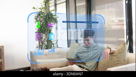 Ein Mann, der ein hellgrünes T-Shirt trägt und zu Hause holographische Karten studiert, mit Pflanzen Stockfoto