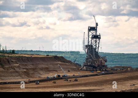 Massiver Schaufelradbagger im Braunkohlebergwerk Hambach bei Kerpen, Deutschland, mit Windturbinen am Horizont. Stockfoto