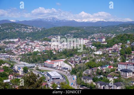 Der Blick von der Aussichtsplattform im oberen Teil des Arboretum Parks auf die Wohngebiete von Sotschi auf dem schneebedeckten Berggrund. Kra Stockfoto