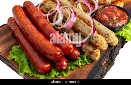 Würstchen werden auf einem Holzbrett mit Salat und Zwiebeln gelegt. Eine kleine Schüssel Soße ist neben den Würstchen. Stockfoto