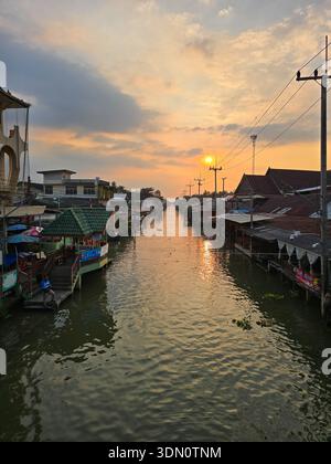 Amphawa Floating Market, Thailand 5. Dezember 2025. Besucher genießen lokale Speisen und Kunsthandwerk entlang des ruhigen Kanals, während die Sonne untergeht und ein warmes Licht ausstrahlt Stockfoto