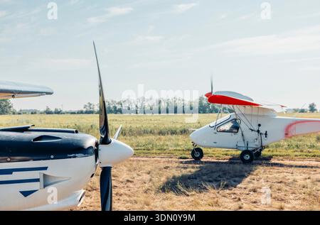Zwei Flugzeuge parkten auf einem Farmfeld. Das eine ist ein kleines weißes Flugzeug mit einem roten Streifen, das andere ist ein schwarzes und weißes Flugzeug. Der Hintergrund Stockfoto