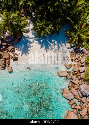 Erleben Sie die Ruhe von Anse Lazio in Praslin, Seychellen, wo sanfter Sand auf azurblaues Wasser trifft. Üppige Palmen spenden Schatten, während die Strandgäste mich tränken Stockfoto