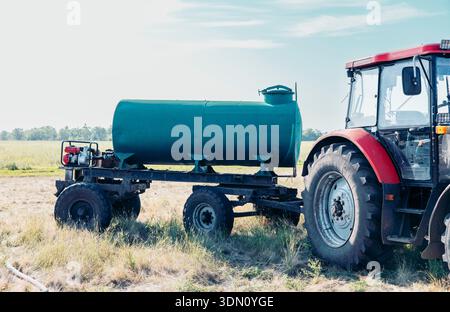 Roter landwirtschaftlicher Traktor auf dem ländlichen Feld mit Wassertank-Anhänger unter blauem Himmel geparkt, offene Landschaft mit großem Banner für Kopierraum Stockfoto