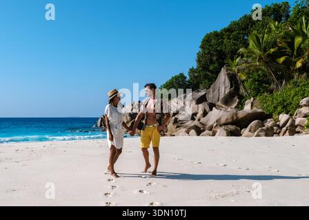 Ein fröhliches Paar geht Hand in Hand auf dem weichen weißen Sand von Anse Cocos, umgeben von üppigem Grün und kristallklarem türkisfarbenem Wasser. Die Sonne Stockfoto