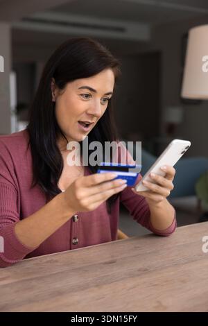 Latina sieht erstaunt aus, während sie Kreditkarte und Smartphone hält Stockfoto