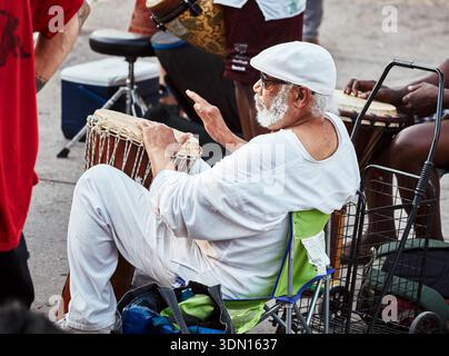 Montreal, Kanada – Juni 2018: Älterer Mann mit weißem Bart und Mütze sitzt und spielt aktiv eine Djembe-Trommel während einer Outdoor-Community-Musiksession Stockfoto